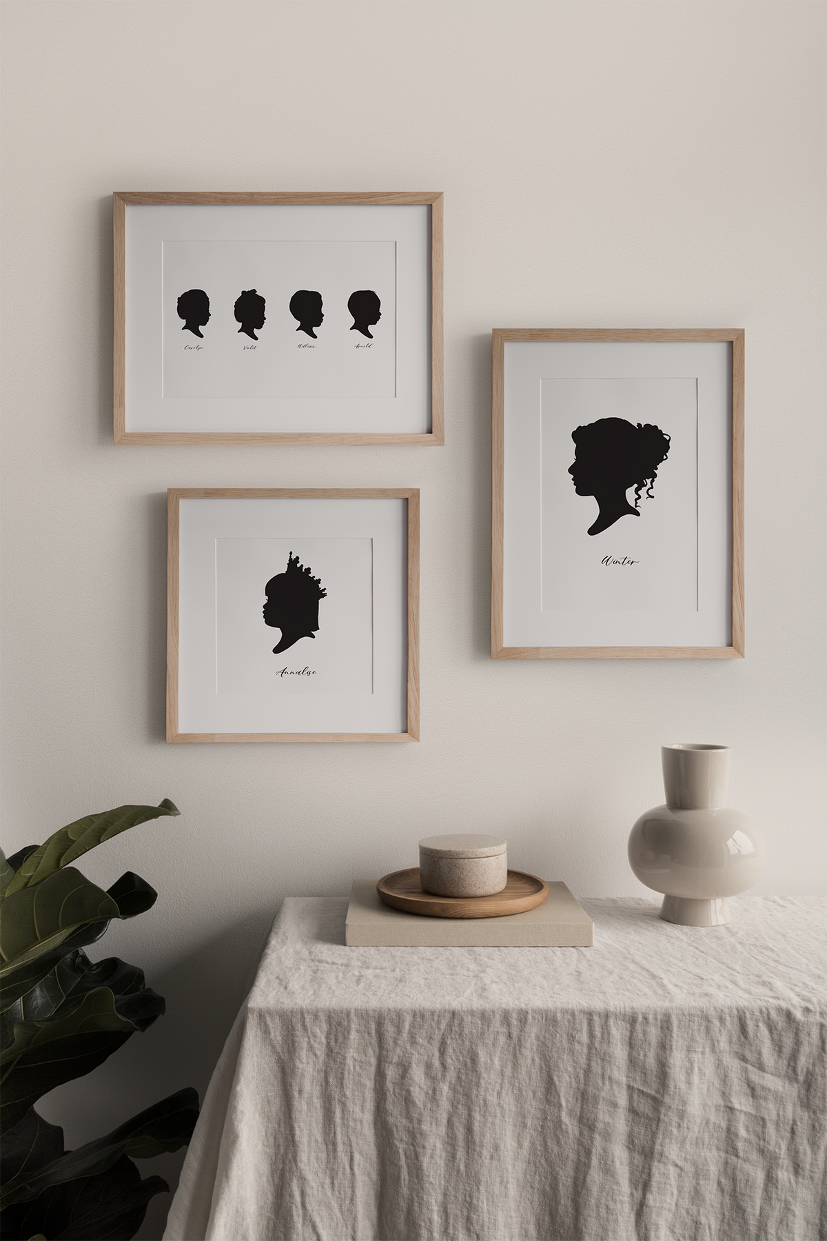 Three framed Custom Hand-Drawn Silhouette Portraits hanging on a wall above a table.